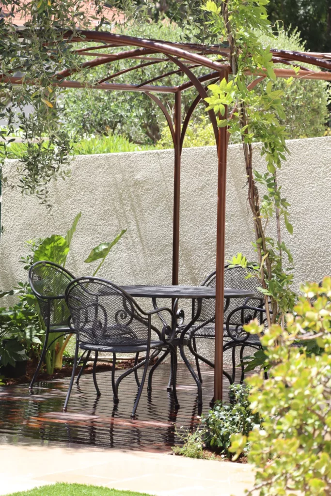 Pergola couverte de végétation avec table et chaises dans un patio extérieur