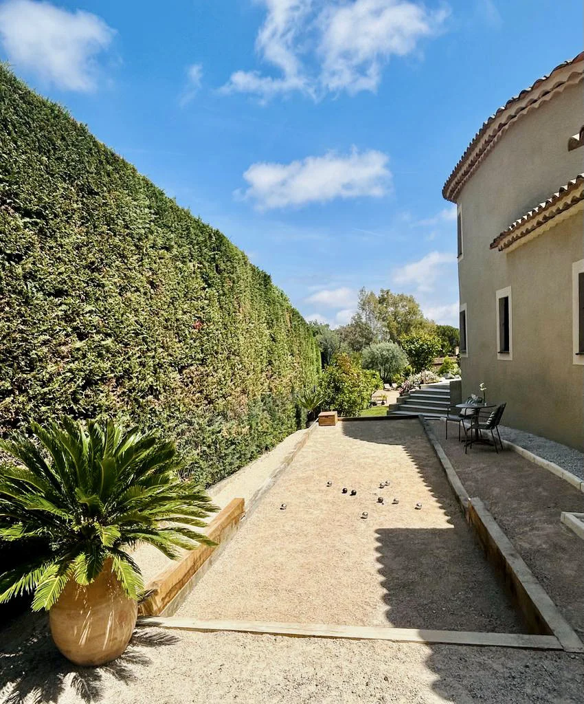 Cour ensoleillée avec une haie taillée, une zone de gravier, des plantes en pots et un espace de détente.