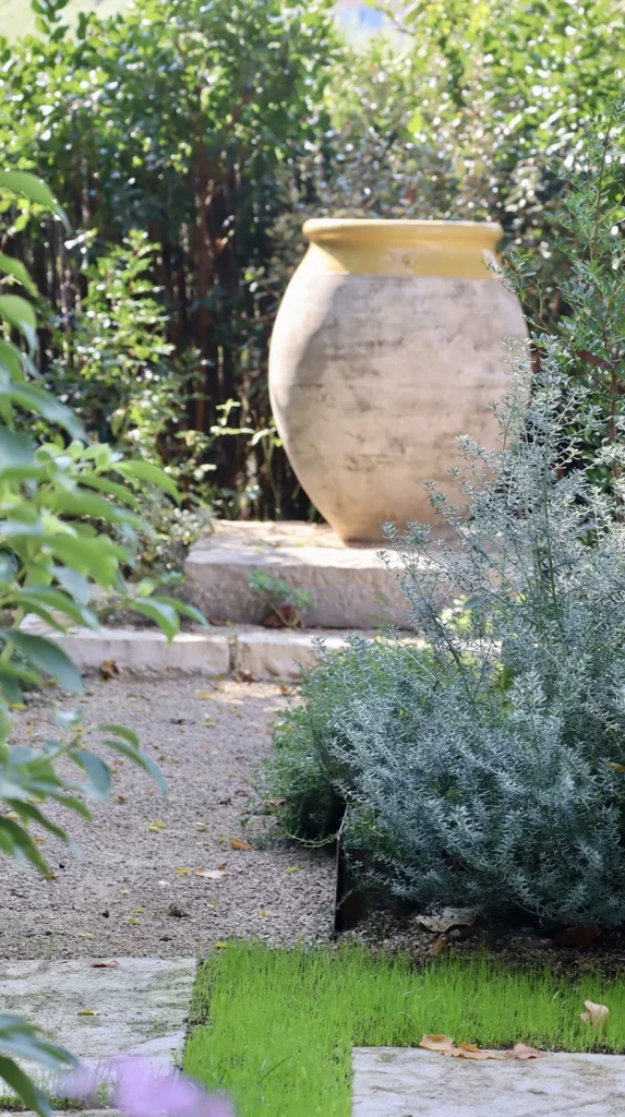Grande urne de jardin patinée posée sur une marche en pierre, entourée de plantes