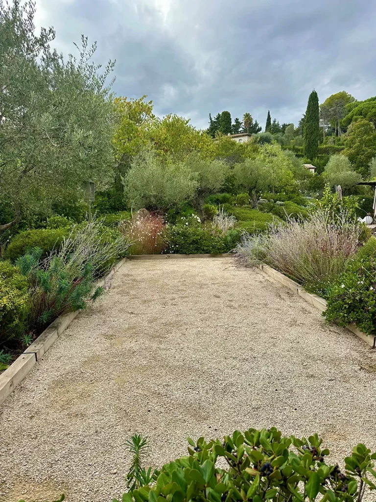 Allée de jardin en gravier beige bordée de massifs plantés, d’arbustes et de fleurs.